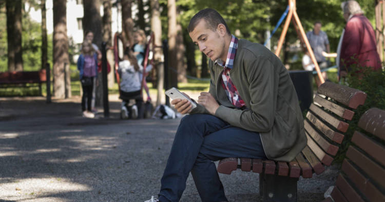 Puisto Helsingin Myllypurossa. Nuori mies istuu penkillä ja käyttää kännykkää. Kuvassa Maged Muhaisen Jose.